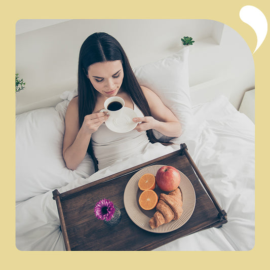 a woman drinking coffee on her bed