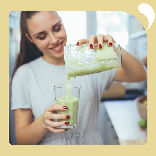 a woman smiled and poured the green milkshake from the blender into the cup