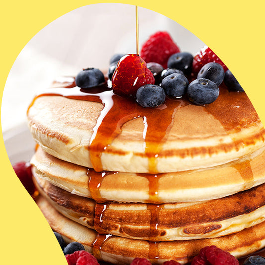 syrup being poured on fluffy pancakes and surrounded by raspberries and blackberries