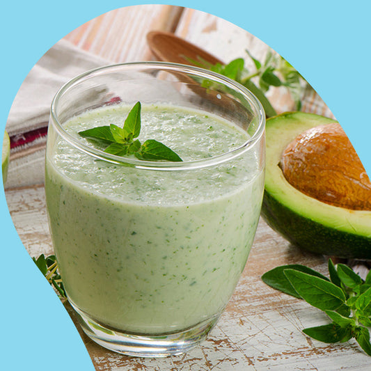 kale smoothie a in glass cup next to a half cut avocado