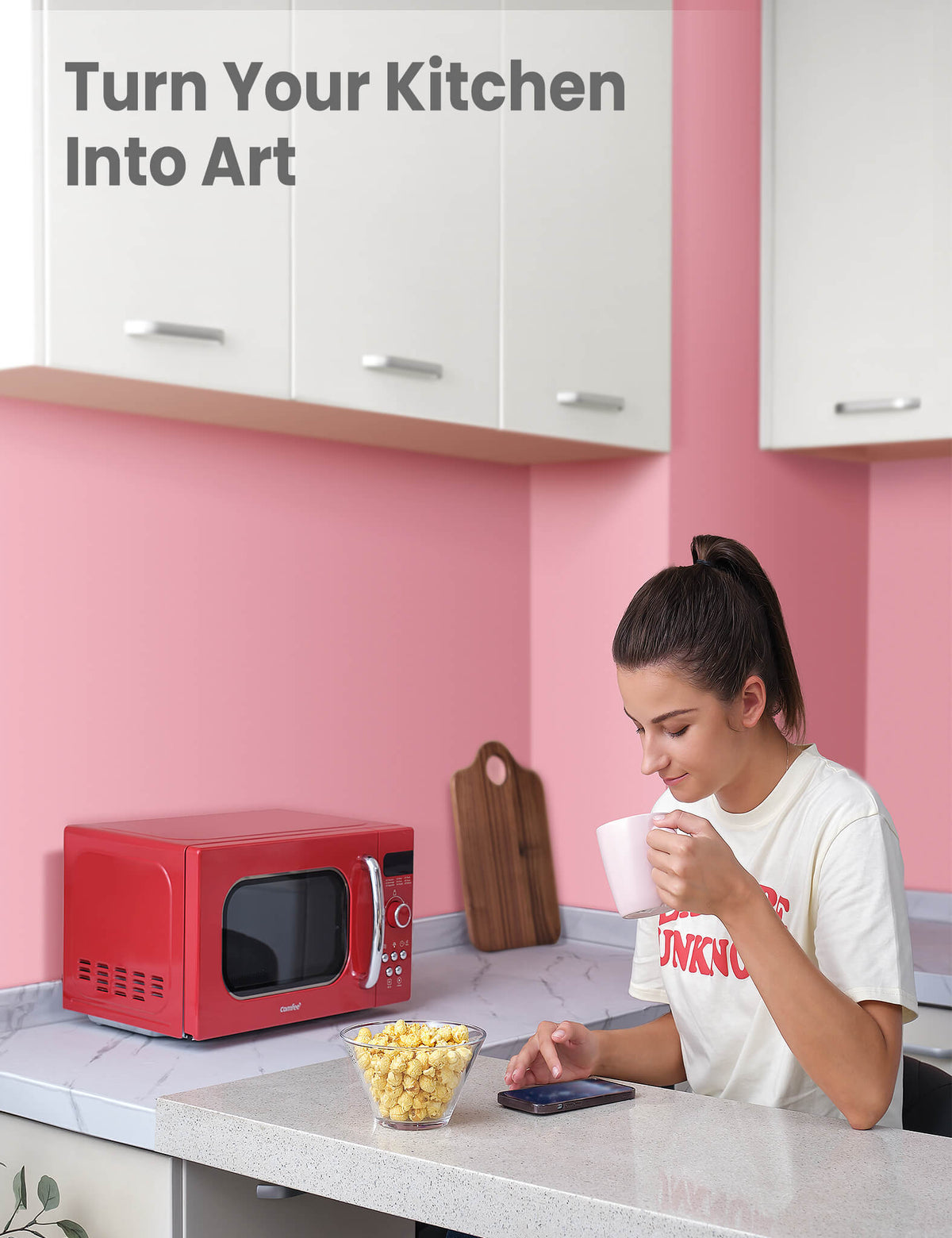 A woman with a glass of water looking at her phone, popcorn in front of her, and a red microwave oven next to her